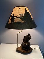 Lamp showing fishing scene silhouette on shade when lit, fish sculpture on wooden base.