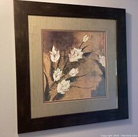 Front view of framed artwork featuring white flowers and fabric bordered matting in dark brown frame.