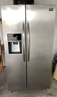 Front view showing stainless steel side by side refrigerator with water and ice dispenser on left door. Visible ding on front right door.