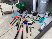 Wide view of gardening tools, seed spreader, metal can, irrigation equipment, gloves, and shade cloth on driveway