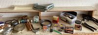 Wide view of assorted home repair supplies on shop bench including metal L-brackets, wooden strips, wire coil, and containers of screws.