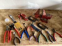 Full view of the hobby tool collection showing various pliers, vises, glass cutters, and small tools on plywood surface.