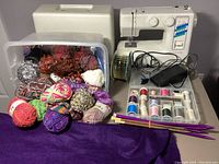 Janome sewing machine, assorted yarn balls, spools of thread, knitting needles, and foot pedal grouped on table