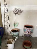 Photo of lot showing two mosaic pots, white watering can, terracotta pot, metal trellis, and decorative butterflies.