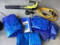 Overview photo of Ryobi 18V leaf blower, charger, yellow extension cord, and multiple blue tarps folded on floor.