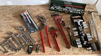 Wide shot of entire collection including pipe wrenches, adjustable wrench, socket sets with ratchets, crescent wrenches and Allen wrenches laid out on plywood.