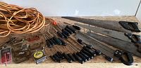 Photo showing three hand saws, many screwdrivers, clamps, tape measure, pliers and an orange extension cord on a wooden surface