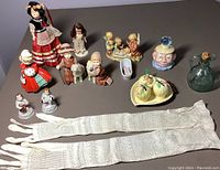 Wide top view showing all dolls, figurines, ceramic apples on plate, glass pitcher, caricature face, and two pairs of white lace gloves.