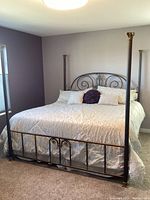 Full view of king size hand forged metal bed frame with bedding, showing ornate scrollwork and gold accents on posts and headboard/footboard.