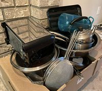 Cookware and kitchen items packed with visible pots, pans, kettle, strainers, and a blue water bottle.