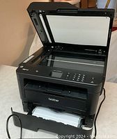 Front view with scanner lid open showing flatbed glass, control panel, output drawer and loaded paper tray