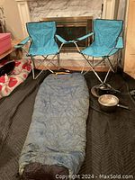 Photo showing two blue folding camping chairs, a blue North Face sleeping bag laid out on the floor, and three pieces of cookware including a fry pan, large pot, and small pot.