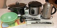 Full view of all kitchen items including slow cooker, rice cooker, kettle, strainer, utensils, cutlery, cutting boards, and Starbucks cup.