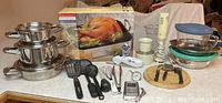 Overview of lot showing cookware stack, turkey roaster box, mixer, utensils, thermometers, cheese board, and Pyrex bowls