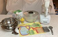 Full view of all kitchen items including colander, lemon squeezer, salad spinner, food processor, grater, vegetable peeler, and kitchen helper tool.