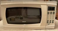 Front view of beige RCA microwave oven with glass window and keypad