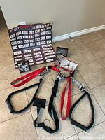 Workout pulley system with connected red and black straps and padded handles, instructional poster behind showing exercise steps and images.