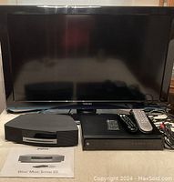 Front view of Toshiba TV with Bose Wave Music System III, Motorola PVR, remotes, and Bose manual on table.