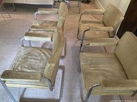 Front perspective showing all four chairs arranged in pairs on carpet, beige leather seats and chrome frames