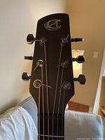 Headstock close-up showing Composite Acoustics logo and sealed chrome tuning machines on carbon fiber surface.