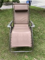 Front view of the light brown anti-gravity lounger showing fabric seating with suspension cords and cushioned headrest pillow.