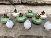 Six coal oil lamps (four green, two white) arranged in two rows with three white glass shades in front on stone surface