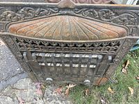 Angled top view of the antique cast iron electric fireplace insert highlighting the rounded, fan-like top panel with floral and scrollwork around the edges, visible rust and weathering.