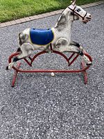 Side view of the antique metal ride-on toy horse showing white body with black detailing, blue saddle with yellow trim, and red metal rocking frame.