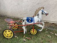 Side view of the antique metal ride-on horse showing the white horse with blue saddle marked with number 2, yellow wheels, and red metal frame with pedals.