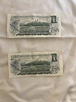 Front and back view of two circulated Canadian one dollar bills featuring Queen Elizabeth II and Ottawa Parliament buildings.