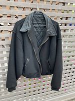 Front view of black wool jacket with leather collar and zip closure displayed on hanger