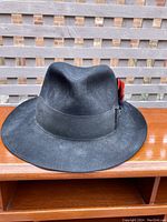 Front view showing black felt hat with slight dust and a red feather decoration on hatband.
