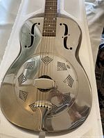 Close-up of nickel-plated resonator cone, cover plate and F-holes on guitar body.