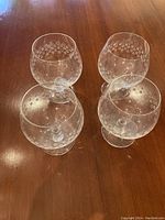 Four Rosenthal brandy snifter glasses with etched floral design arranged on a wooden table.