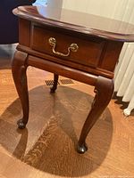 Wooden Huppe side table with cabriole legs and single drawer with brass handle from a frontal angle.