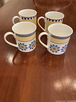 Four Villeroy and Boch coffee mugs sitting on a wooden table showing the floral and stripe Twist pattern.