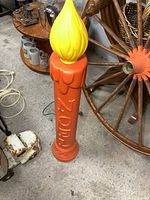 Full view of vintage Nortel blow mold candle light standing on floor near wooden wagon wheel and other collectibles.