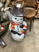 Front-facing full view of vintage blow mold snowman showing hat, scarf, and penguin with holiday attire.