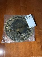 Brass sundial sealed in clear plastic packaging, 8-inch diameter, Roman numerals, and inscription visible.