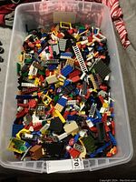 Large clear plastic bin filled with mixed colorful building blocks of various types and sizes