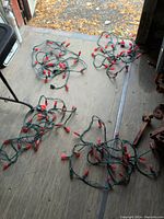 Four separate strands of red LED Christmas lights laid out on a concrete floor surface, showing length and bulb spacing.