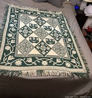Full view of the rectangular Christmas throw laid flat on a bed, showing its geometric star and floral pattern in green and beige with fringed edges.