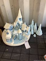 Top-down view of the Christmas village set showing 4 buildings, clock tower, pine trees, carolers, and snowy cobblestone base.