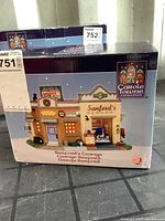 Front photo of box showing the image of the Sanford's Garage porcelain collectible building from the Carole Towne Collection Christmas Village series.
