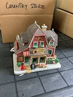 Front and side view of Luannes Coffee House collectible Christmas Village building with detailed façade, potted plants, and signage.