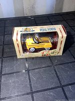 Front-side view of boxed yellow diecast NYC cab pedal car showing packaging and car details.
