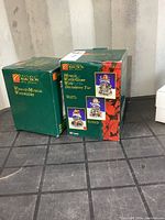 Two green boxes labeled Musical Water Globe and Wind-up Musical Water Globe standing side by side on a black surface