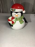 Front view of penguin cookie jar with red Santa hat, green scarf, and peppermint candy decoration on belly.