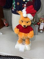 Front view of Winnie the Pooh plush figure wearing Santa hat and red shirt on melted white base.