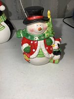 Front view of ceramic snowman cookie jar showing detailed facial features, scarf, jacket, and attached small penguin.